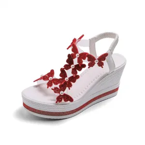 Détail de sandales compensées blanches avec décorations de papillons rouges et perles