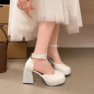 Gros plan sur des chaussures Mary Jane en verni blanc avec talons épais et strass.