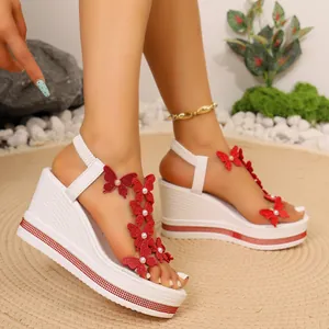 Détail rapproché de sandales compensées blanches avec papillons rouges et perles