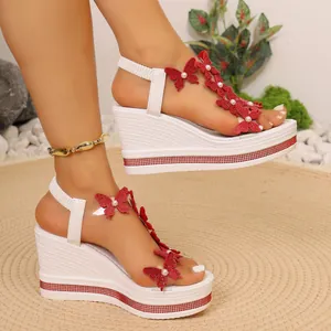 Détail de sandales compensées blanches avec papillons rouges, perles et bordure strass.