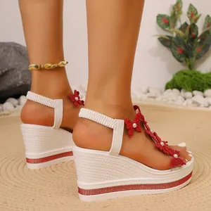 Détail des sandales à talons compensés blanches avec papillons rouges et perles.