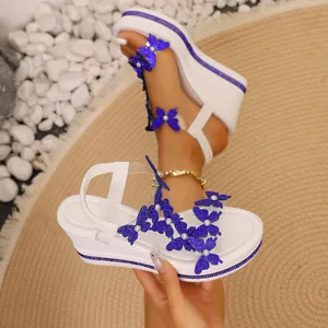 Détail de sandales compensées blanches avec papillons en strass bleus et perles.