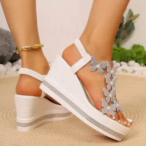 Détail de sandales compensées blanches avec perles papillon et bordure en strass