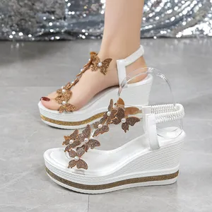 Detailed view of white wedge sandals featuring golden butterfly, pearls, and rhinestone accents