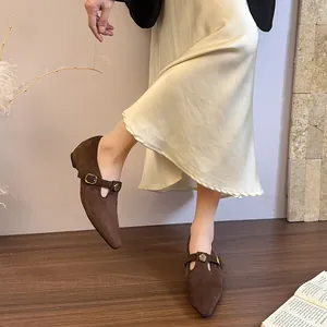 Dettaglio di scarpe Mary Jane in pelle scamosciata marrone con punta e fibbia a rosa d'oro.