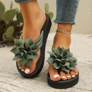 Primer plano de chanclas de mujer con flor grande de tela verde en suela negra.