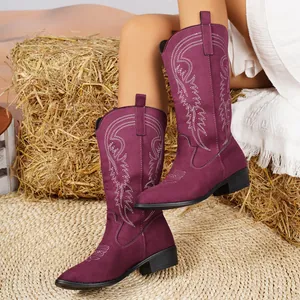 Gros plan sur des bottes de cow-boy bordeaux avec broderies blanches sur foin.