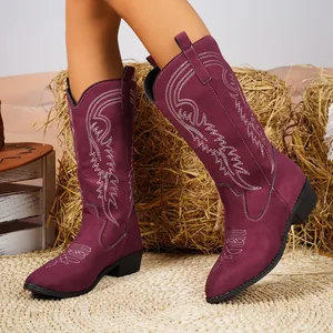 Gros plan de bottes de cowboy en daim bordeaux avec broderies blanches et coupe en V classique.
