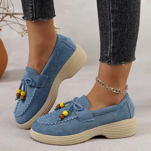 Close-up van blauwe suède platform loafers met strik en kralen op het model.