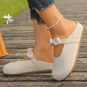 Close-up of stylish beige Mary Jane mule clogs featuring a bow strap and soft suede texture