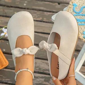 Detailed view of beige Mary Jane clogs with bow strap on rustic wooden background