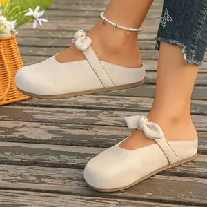 Detailed view of women's beige summer mule sandals with cute bow detail on wooden deck