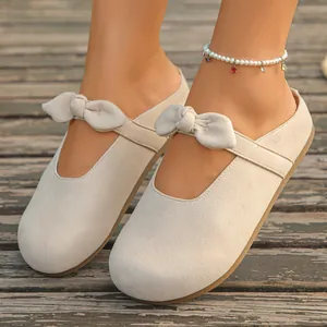 Close-up of beige suede-like casual flat slippers with bow detail on a wooden deck