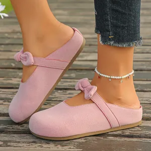 Close-up of pink suede Mary Jane mules with bow detailing on a wooden deck