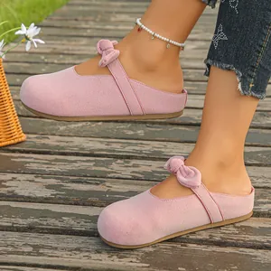 Stylish pink suede Mary Jane mules with bow detail worn on a rustic wooden deck