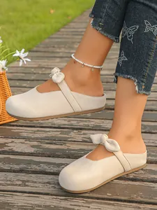 Detail of beige suede mules featuring an elegant bow-knot strap and comfortable sole.