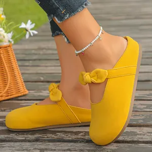 Close-up view of vibrant yellow Mary Jane mule sandals with bow detail on wooden deck