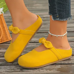 Close-up of yellow suede bow mules worn with a pearl anklet on wooden deck