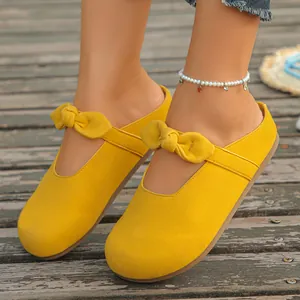 Close-up detail of yellow summer mules with decorative bow knot worn on wooden deck