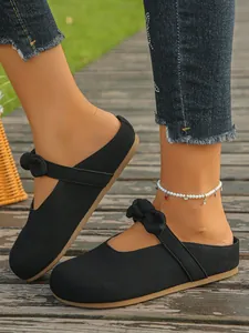 Detailed shot of black canvas mule slippers with stylish bow strap on wooden boardwalk