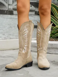 Detail shot of beige suede western tall boots with intricate white wing embroidery