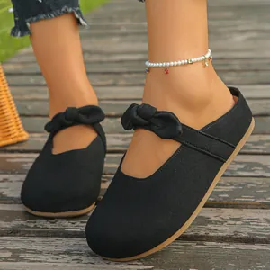 Detailed view of women's black slip-on mule sandals with knot strap on rustic wood