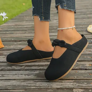Detailed close-up of black mule slippers with elegant bow on a wooden walkway