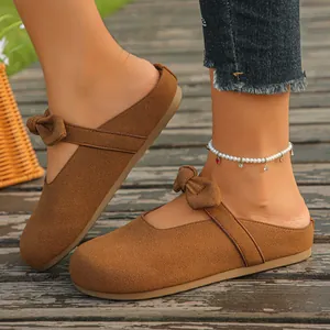 Detail of stylish brown suede slip-on mules featuring a cute bow strap on wooden deck