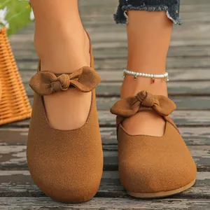 Detailed close-up of brown suede Mary Jane sandals with bow accent on wooden deck