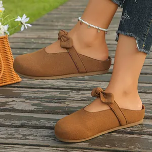 Detailed view of stylish brown suede bow mules for women on a rustic wooden deck