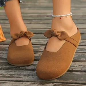 Close-up of brown suede Mary Jane mules with decorative bow and foot accessory