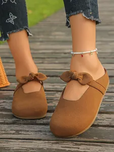 Close-up detail of women's brown suede Mary Jane mules with bow on wooden deck
