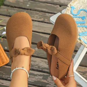 Close-up of brown suede clogs with decorative bow on a wooden outdoor background