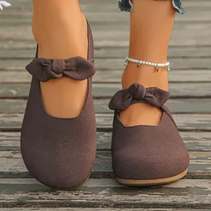 Close-up of stylish brown suede Mary Jane clogs with a bow knot on a wooden deck