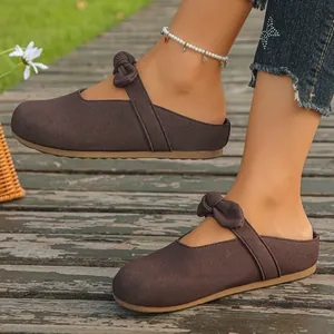 Casual brown suede Mary Jane mules with elegant bow strap detail on a wooden path.
