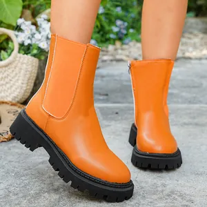 Gros plan de bottines Chelsea orange vif avec semelles crantées noires et fermeture.
