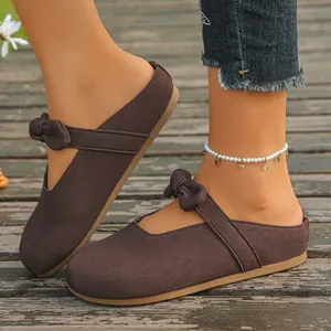 Detailed close-up of women's brown suede slip-on mules featuring a chic decorative bow strap