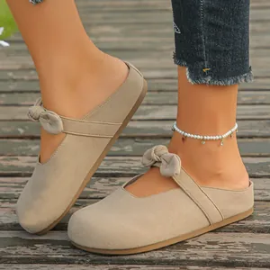 Detail shot of stylish beige suede mule clogs with elegant bow strap on wooden deck