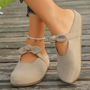 Close-up of stylish beige suede bow mules for women on a rustic wooden floor.