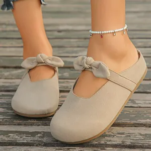 Detailed view of beige suede mule sandals featuring a cute bow on a wooden deck.