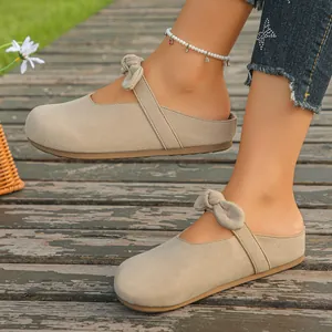 Close-up of stylish beige mule sandals with bow detail worn on a rustic wooden deck