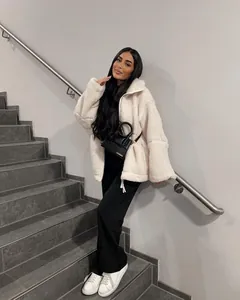 Modell trägt eine lockere, cremefarbene Fleecejacke auf einer modernen, grauen Treppe.