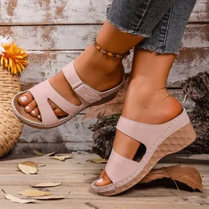 Detalle de sandalias de cuña rosas con tiras huecas sobre un fondo rústico de madera.