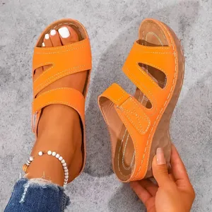 Primer plano de sandalias con cuña naranjas para mujer con costuras blancas decorativas