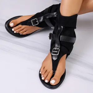 Close-up of black flat gladiator sandals with thong toe and buckle straps details.