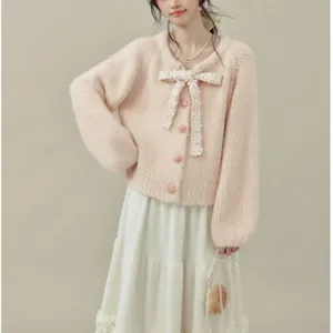 Cardigan rosa in maglia morbida con un delicato fiocco di pizzo bianco e texture soffice.