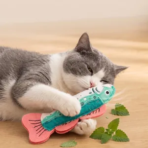 Grau-weiße Katze spielt mit einem bunten Plüschfisch-Katzenminze-Spielzeug auf Holz