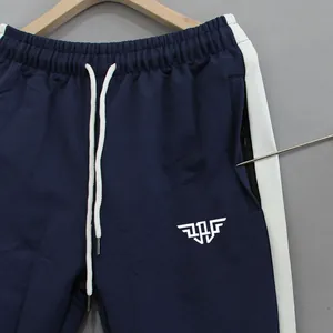 Detail shot of navy sports pants with white side stripes and zipper pocket feature.