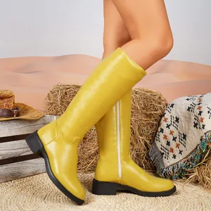Seitenansicht leuchtend gelber kniehoher Stiefel an einem Modell in Wüstenumgebung.