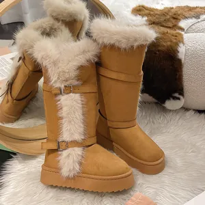 Detail view of tall tan snow boots with faux fur trim and buckle straps on a white rug